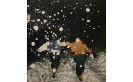Zwei Personen laufen durch Schnee, beleuchtet von hellem Licht. Flocken schweben in der Luft, es wirkt wie ein Schneesturm.