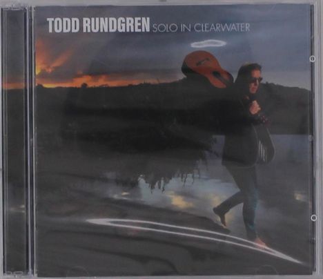 Text: "Todd Rundgren Solo in Clearwater". Mann mit Gitarre über der Schulter vor Sonnenuntergang am Wasser.