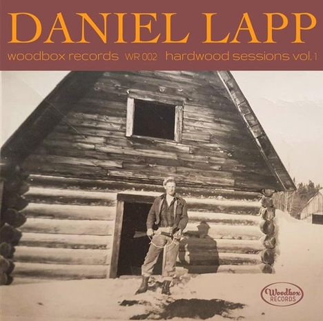 "Daniel Lapp. Woodbox Records WR002. Hardwood Sessions Vol. 1." Ein Mann steht vor einer Holzblockhütte im Schnee.
