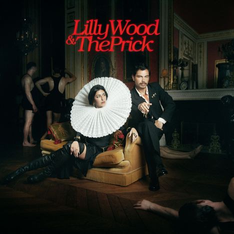Text: "Lilly Wood & The Prick" in Rot. Zwei Personen auf einem Sofa in einem eleganten Raum, mit Leuten im Hintergrund.