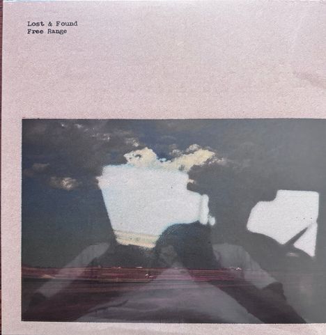 Text oben: "Lost & Found Free Range". Darunter eine Landschaft mit blauem Himmel und Wolken, reflektiert im Fenster.