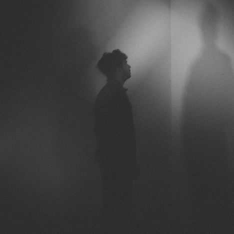 Es gibt keinen Text zu erwähnen. Silhouette eines Mannes, der in einem düsteren Raum in Richtung einer Wand schaut.