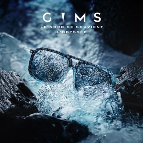 "GIMS, LE NORD SE SOUVIENT, L'ODYSSÉE." Eine Sonnenbrille liegt auf eisigen Steinen mit Wasser.