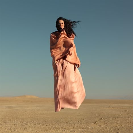 Ich kann keine spezifischen Texte oder Namen erkennen. Eine Person in einem fließenden rosa Kleid steht in einer Wüstenlandschaft.