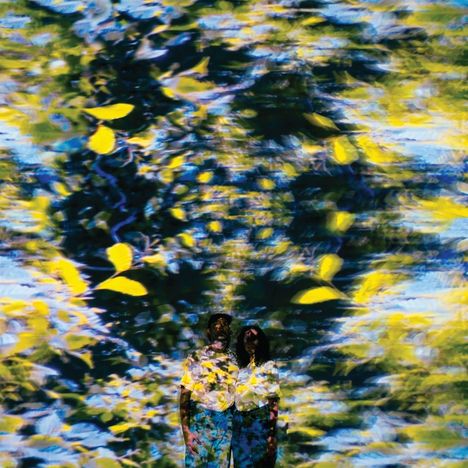 Zwei Personen vor verschwommenem Hintergrund aus gelben und grünen Blättern mit blauen Akzenten.