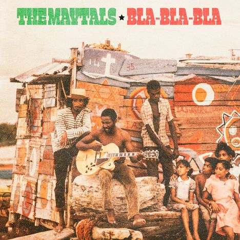 "The Maytals Bla-Bla-Bla." Eine Gruppe von Menschen vor einer bemalten, rustikalen Behausung, ein Mann spielt Gitarre.