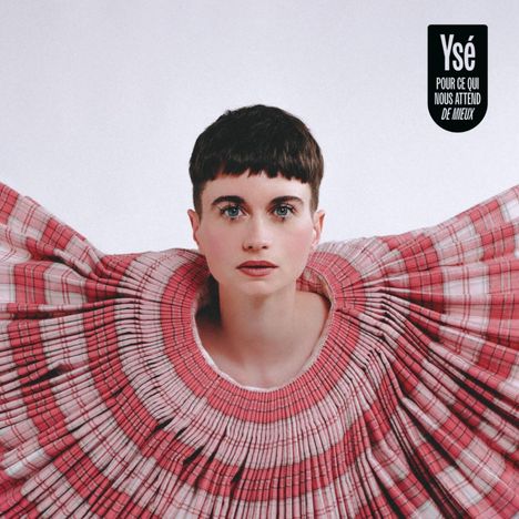 Texte: "Ysé, POUR CE QUI NOUS ATTEND DE MIEUX." Frau mit kurzem Haar trägt ein weit ausgebreitetes, plissiertes Kleid in Rosa-Tönen.