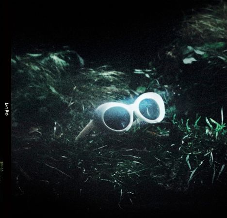 Der Text ist nicht erkennbar. Zu sehen ist eine weiße Sonnenbrille auf dunklem, verworrenem Hintergrund.