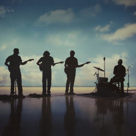 Silhouetten von vier Musikern: drei mit Gitarren, einer am Schlagzeug, vor einem Himmel mit Wolken im Hintergrund.