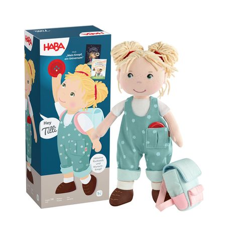 HABA, Hey Tilli, inklusive Rucksack und Wunschknopf. Stoffpuppe mit blonden Haaren und blauer Latzhose. Box im Hintergrund.