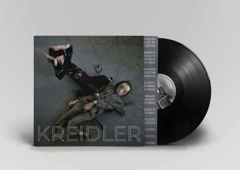 Text: „SCHEMES“ und „KREIDLER“. Zwei Puppen mit Drähten und Löffeln auf einem Boden liegend.