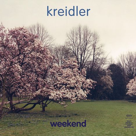 „kreidler“ oben, „weekend“ unten. Blühende Bäume mit rosa Blumen in einer grünen Wiese.