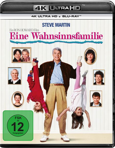 Text: "Eine Wahnsinnsfamilie", "FSK ab 12 freigegeben". Ein Mann hält zwei Kinder kopfüber; mehrfach gerahmte Fotos im Hintergrund.