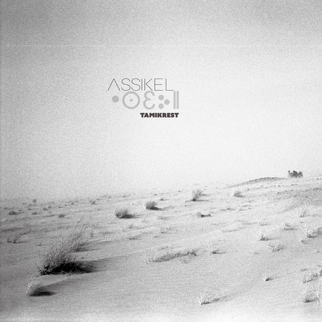 Text: "ASSIKEL Tamikrest". Eine monochrome Wüstenlandschaft mit vereinzelten Büschen.