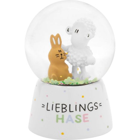 "LIEBLINGS HASE" steht auf einem Schneekugel-Sockel mit Hase und Schaf in der Kugel, umgeben von buntem Konfetti.
