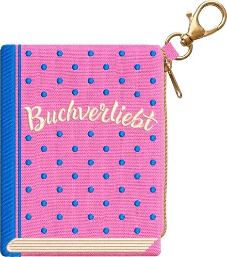 „Buchverliebt" steht auf einer pinken, gepunkteten Tasche mit blauem Rand und goldfarbenem Schlüsselanhänger.