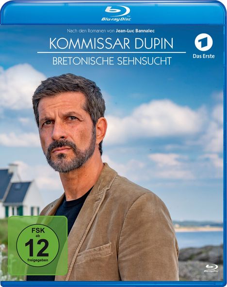 "Kommissar Dupin: Bretonische Sehnsucht", FSK ab 12. Ein Mann mit Bart in braunem Sakko, Häuser im Hintergrund, blauer Himmel.