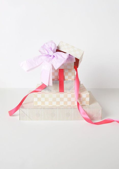 Beige karierte Boxen; oben eine geöffnete Box mit rosa Schleife und Band. Eleganter Stapel vor weißem Hintergrund.