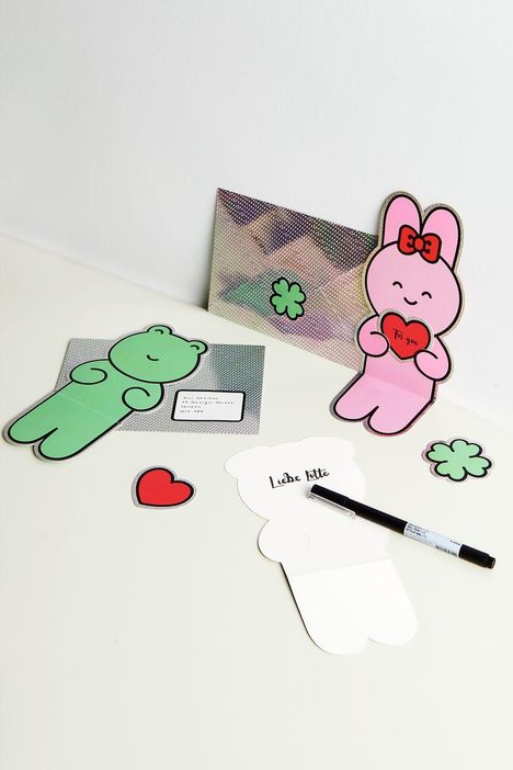 Eine Illustration mit Notizen: "To you" auf rotem Herz, "Liebe Lotte" auf Papier. Bär und Hase als Figuren mit Kleeblättern.