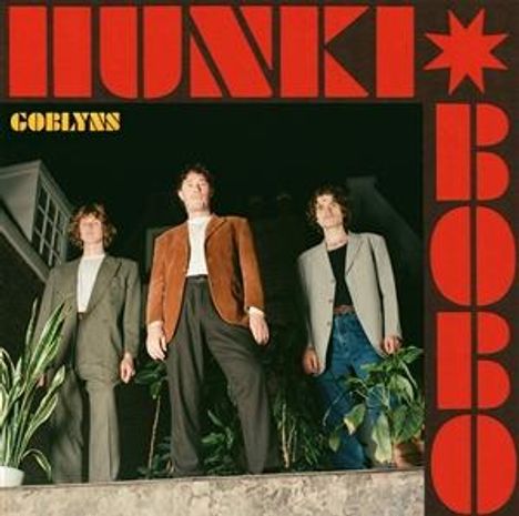 Hunki Bobo, Goblyns. Drei Personen in Anzügen stehen draußen vor einem Gebäude mit Pflanzen.