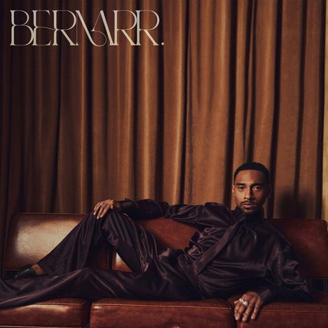"BERNARR." Oben links. Eine Person in eleganter Kleidung liegt entspannt auf einem Ledersofa vor braunem Vorhang.