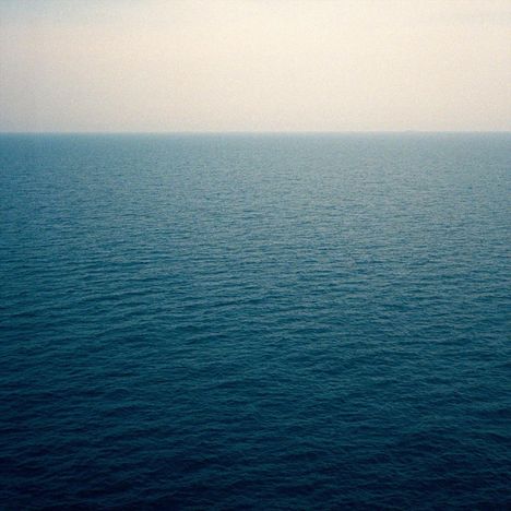 Ein ruhiger, blauer Ozean erstreckt sich bis zum Horizont unter einem hellen, wolkenlosen Himmel.