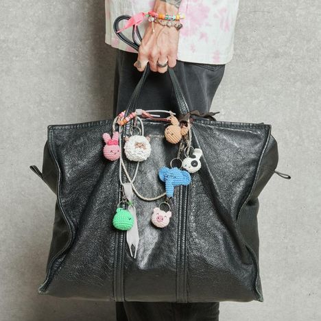 Eine schwarze Ledertasche mit mehreren bunten, gehäkelten Anhängern in Tierformen. Eine Hand hält die Tasche.