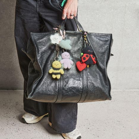 Eine schwarze Tasche mit niedlichen, gehäkelten Anhängern: Biene, Wolke, Herz, Marienkäfer und Figur.