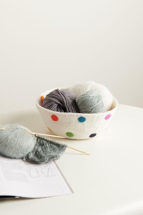 Eine Schale mit bunten Punkten, gefüllt mit Garnknäueln. Davor liegt ein Strickprojekt auf einer Anleitung.