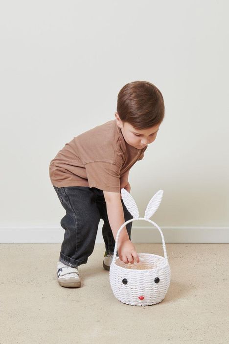 Ein Kind in braunem Shirt greift in einen weißen Korb mit Hasenohren und Gesicht.