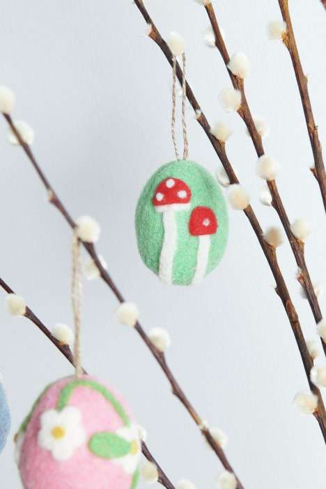 Zwei bemalte Ostereier hängen an Zweigen. Eines hat rote Pilze auf grünem Grund, das andere weiße Blumen auf rosa Grund.