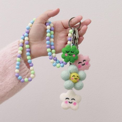 Bunte Perlenkette mit Filzanhängern in Blumen- und Sternform, alle mit lächelnden Gesichtern.