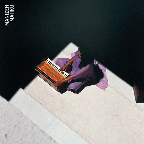 MANIZEH MAHKU. Frau in lila Kleid spielt Harmonium im Schatten auf hellem Boden.