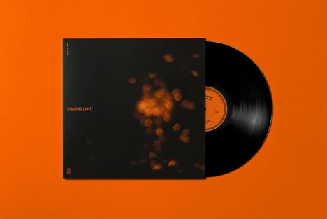 Text: "Chasing Light". Schwarzes Cover mit unscharfen orangenen Lichtpunkten neben einer Schallplatte auf orangefarbenem Hintergrund.