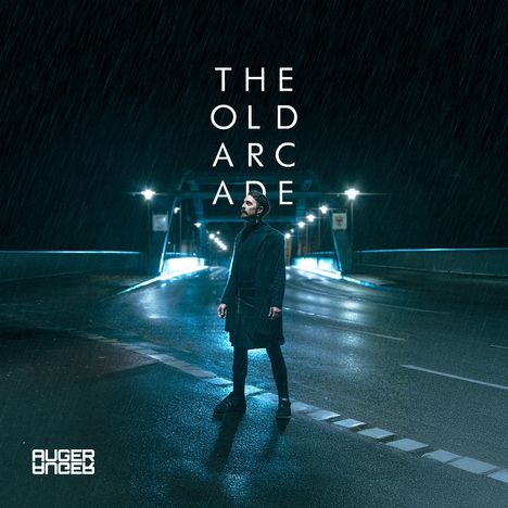 "The Old Arcade" steht groß geschrieben. Eine Person steht nachts auf einer nassen, leeren Straße unter Regen.