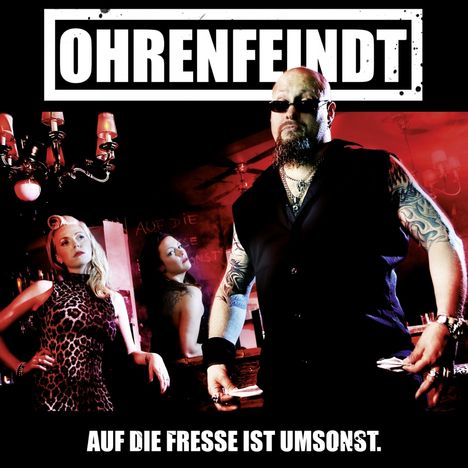 Text: "OHRENFEINDT", "AUF DIE FRESSE IST UMSONST." Ein Mann mit Sonnenbrille und Tattoos steht vor zwei Frauen.