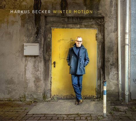 "MARKUS BECKER WINTER MOTION" steht über einem Mann vor einer gelben, abgenutzten Tür in einer alten Mauer.