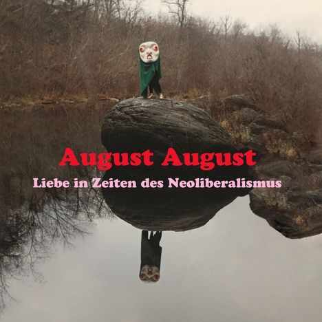"August August: Liebe in Zeiten des Neoliberalismus." Eine verkleidete Figur mit Maske steht auf einem großen Felsen am Wasser.