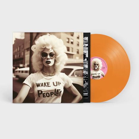 Person mit blonden Locken trägt T-Shirt mit Aufschrift „WAKE UP PEOPLE!“. Orangefarbene Vinyl-Schallplatte daneben.
