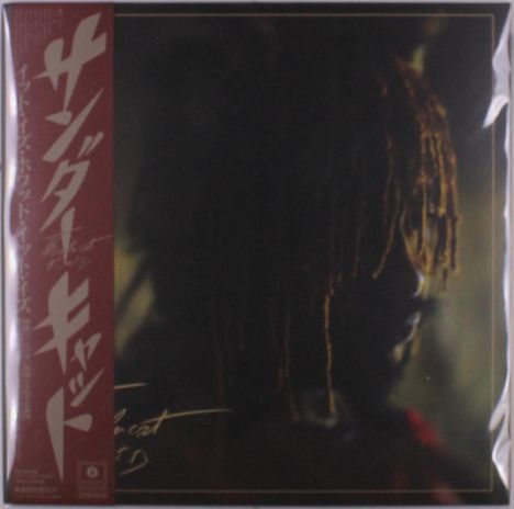 Japanische Schriftzeichen in Weiß auf rotem Hintergrund, seitliches Profil einer Person mit Dreadlocks im dunklen Hintergrund.