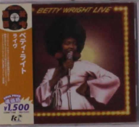 "Betty Wright Live" ist der Text. Eine Sängerin mit Afro trägt ein rosa Outfit und hält ein Mikrofon auf einer Bühne.