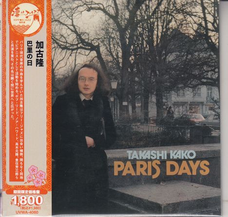 TAKASHI KAKO, PARIS DAYS. Mann in dunklem Mantel steht vor Bäumen, im Hintergrund Gebäude und Autos.