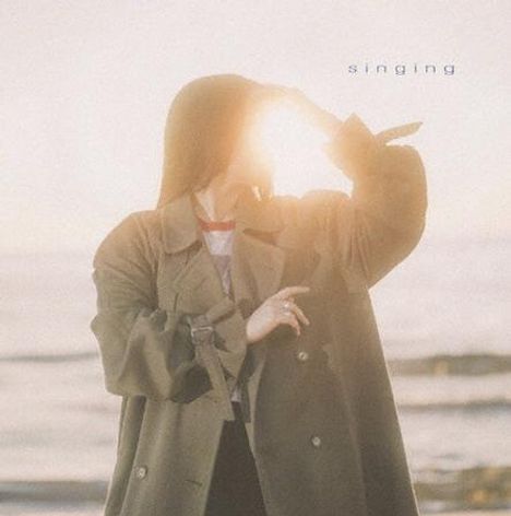 Der Text "singing" steht oben rechts. Eine Person in einem Mantel hält die Hand vor die Sonne an einem Strand.