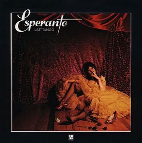 "Esperanto Last Tango" steht oben links. Eine Frau in einem gelben Kleid sitzt entspannt in einem dunklen, stoffbespannten Raum.