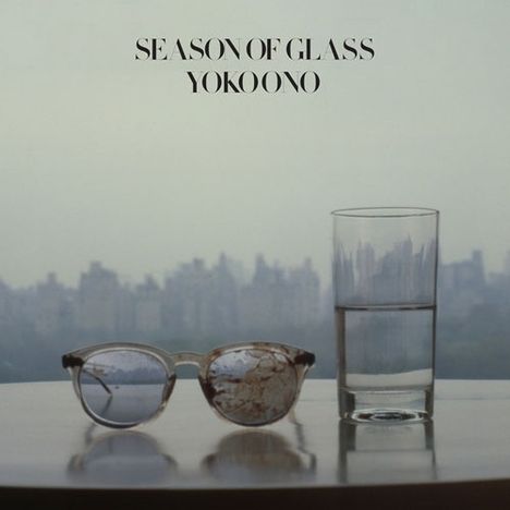 "Season of Glass" und "Yoko Ono" stehen oben. Eine Brille mit Rissen und ein halb volles Glas stehen vor einer Stadtkulisse.