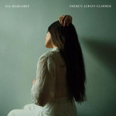 Oben steht "Gia Margaret" und "There's Always Glimmer". Eine Frau sitzt seitlich, Hand auf dem Kopf, langes Haar.