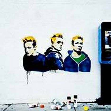 Es gibt keine sichtbaren Texte. Eine Wandmalerei zeigt drei Männer mit gelben Haaren. Davor stehen Farbdosen auf dem Boden.