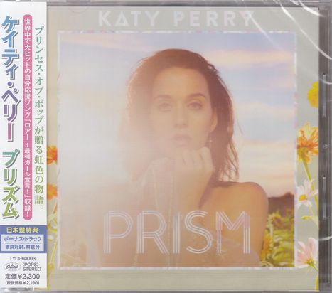 "PRISM" und "KATY PERRY" in weißen Buchstaben. Frau vor Blumenfeld in sanften Farben, Hände am Gesicht.