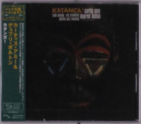 "KATANGA!" gefolgt von Namen. Dunkles, maskenähnliches Gesicht, leuchtende linienartige Akzente. Links japanischer Textstreifen.