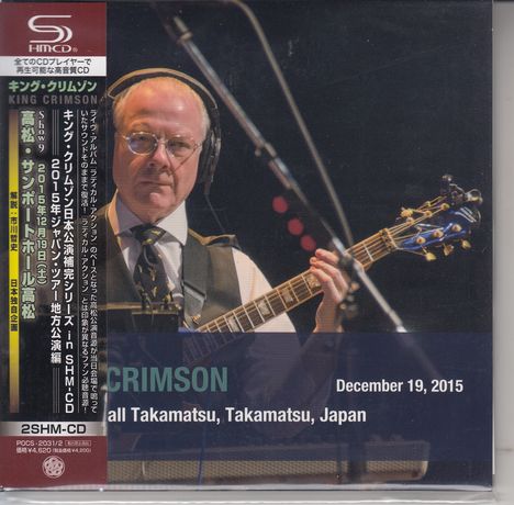 "King Crimson, December 19, 2015, Sunport Hall Takamatsu, Takamatsu, Japan." Ein Mann spielt Gitarre, trägt Anzug und Brille.